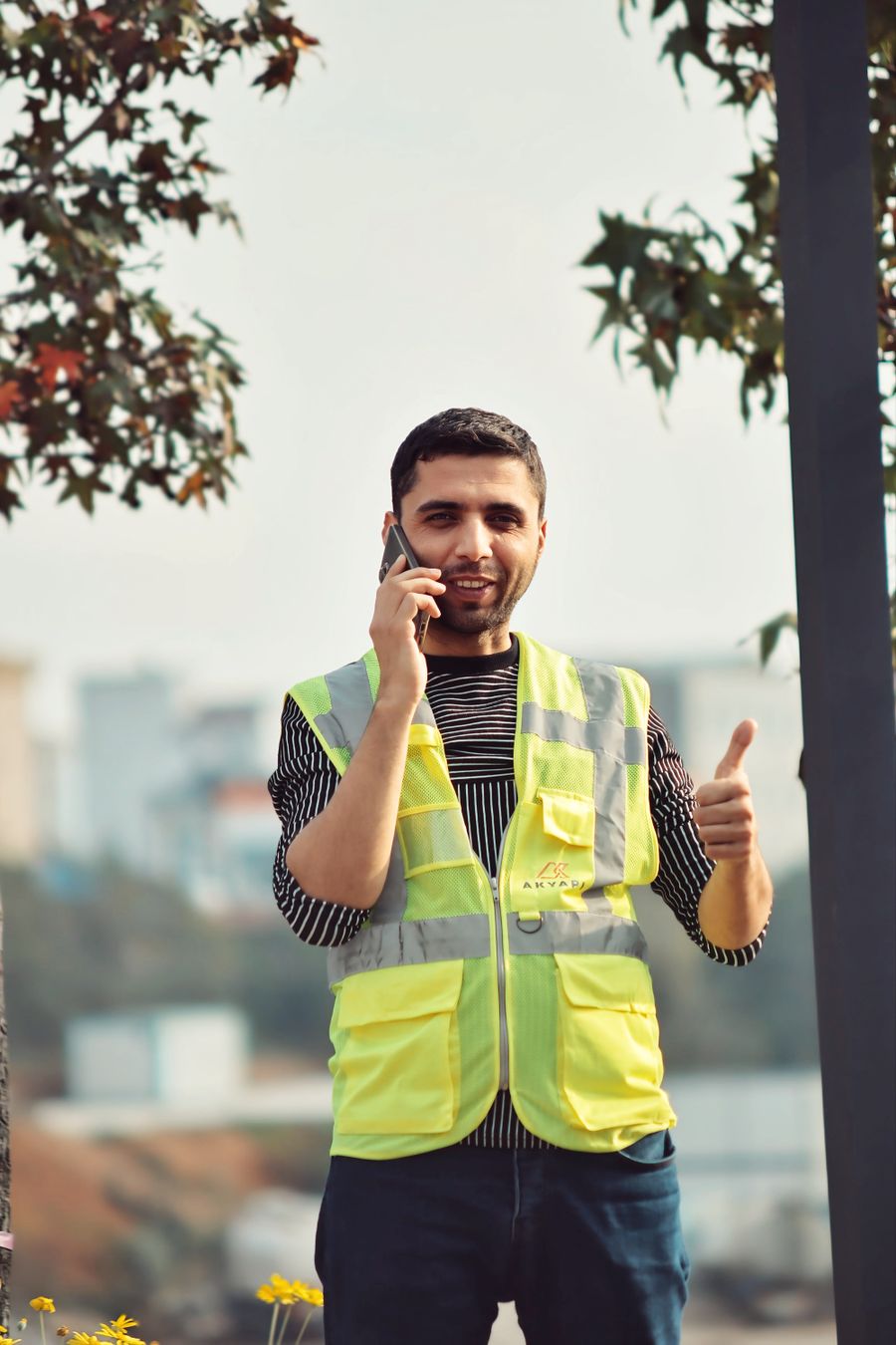 Trabalhador de colete fazendo sinal de positivo enquanto fala ao celular